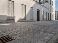 people walking through an old city sidewalk in the sun and shadows on the building windows