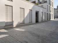 people walking through an old city sidewalk in the sun and shadows on the building windows