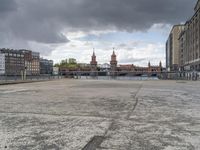 the man is standing on the sidewalk looking out at a canal in the city while a dark cloud is gathering over