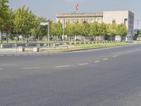 an empty street in front of a building and trees in the middle of the road