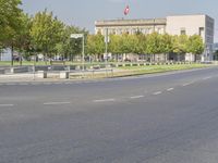 an empty street in front of a building and trees in the middle of the road