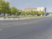 an empty street in front of a building and trees in the middle of the road