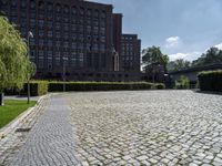 brick walkway in front of a building in front of trees and bushes area of brick floor