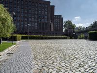 brick walkway in front of a building in front of trees and bushes area of brick floor