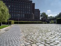 brick walkway in front of a building in front of trees and bushes area of brick floor