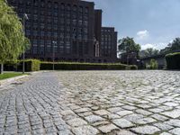 brick walkway in front of a building in front of trees and bushes area of brick floor