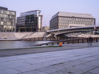 a stone walkway across from some buildings in a city with a bridge crossing over water