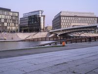 a stone walkway across from some buildings in a city with a bridge crossing over water