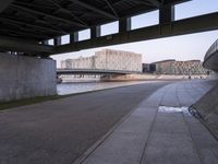 a concrete road passes under a bridge over water and buildings in the city behind it