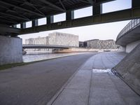 a concrete road passes under a bridge over water and buildings in the city behind it