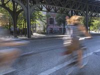 a blurry image of a man on a bike passing a road under a train track