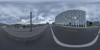 a fisheye photograph of a curved city street in the middle of cloudy day with a building and street light nearby