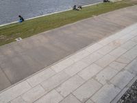 a boy rides a skateboard down a sidewalk near a water feature in the background