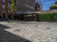 a green shrub near a gray building and a brick walkway with a bicycle rack in it