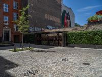 a green shrub near a gray building and a brick walkway with a bicycle rack in it