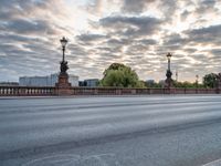 a view of a city street from across a bridge during the evening with cloudy skies