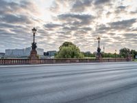 a view of a city street from across a bridge during the evening with cloudy skies