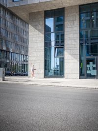 there is a woman standing in the street in front of a building that has glass on it