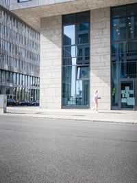 there is a woman standing in the street in front of a building that has glass on it