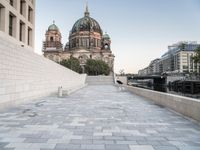 a sidewalk next to a large building with domes and a statue in the center of it