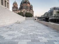 a sidewalk next to a large building with domes and a statue in the center of it