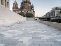 a sidewalk next to a large building with domes and a statue in the center of it