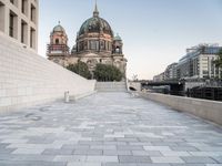 a sidewalk next to a large building with domes and a statue in the center of it