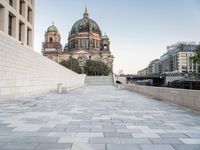 a sidewalk next to a large building with domes and a statue in the center of it