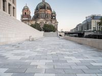 a sidewalk next to a large building with domes and a statue in the center of it