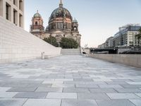 a sidewalk next to a large building with domes and a statue in the center of it