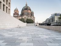 a sidewalk next to a large building with domes and a statue in the center of it