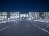 an empty empty road with a building lit up at night behind it in the background