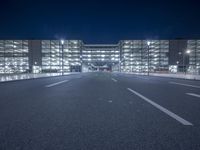 an empty empty road with a building lit up at night behind it in the background