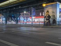 an intersection with many shops in the distance at night time, and a bus passing under an elevated overpass