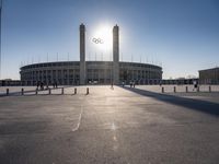 the sun is shining over a large building at an olympics venue with people standing on the sidelines and spectators in the distance