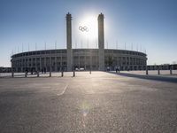 the sun is shining over a large building at an olympics venue with people standing on the sidelines and spectators in the distance