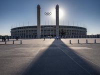 the sun is shining over a large building at an olympics venue with people standing on the sidelines and spectators in the distance