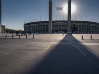 the sun is shining over a large building at an olympics venue with people standing on the sidelines and spectators in the distance