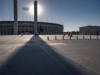 the sun is shining over a large building at an olympics venue with people standing on the sidelines and spectators in the distance