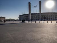 the sun is shining over a large building at an olympics venue with people standing on the sidelines and spectators in the distance