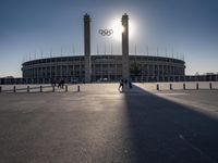 the sun is shining over a large building at an olympics venue with people standing on the sidelines and spectators in the distance