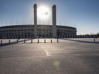 the sun is shining over a large building at an olympics venue with people standing on the sidelines and spectators in the distance