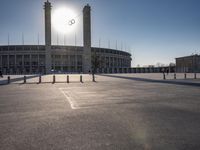 the sun is shining over a large building at an olympics venue with people standing on the sidelines and spectators in the distance