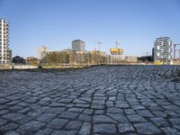 cobblestones near a bridge on the river in the city center of europe with buildings, construction cranes and tall buildings in the background