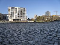 cobblestones near a bridge on the river in the city center of europe with buildings, construction cranes and tall buildings in the background