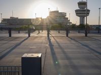 the sun is shining on a city square area with benches and gates near an airplane control tower