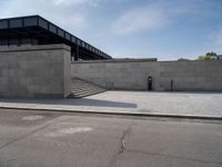 this concrete area contains two steps leading the side of a building to stairs and a large building with concrete walls