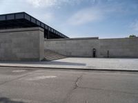 this concrete area contains two steps leading the side of a building to stairs and a large building with concrete walls