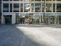 a building with people on bikes near it with tall buildings around it and one person walking on pavement