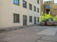 the street with parked cars next to tall buildings has large boulders all around it,